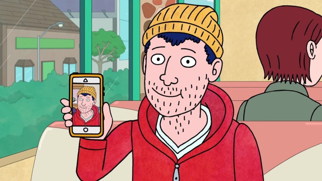 Todd, wearing a yellow beanie and red hoodie, holds up a phone with a picture of him on it, identical to how he looks