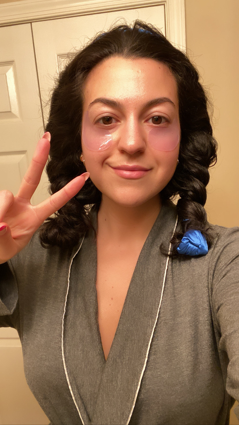 The author wearing a grey robe, hair wrapped in a ribbon, and under eye patches doing a peace sign