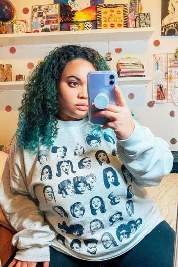 BuzzFeed shopping editor wearing a gray sweatshirt with a print of multiple female rappers on it