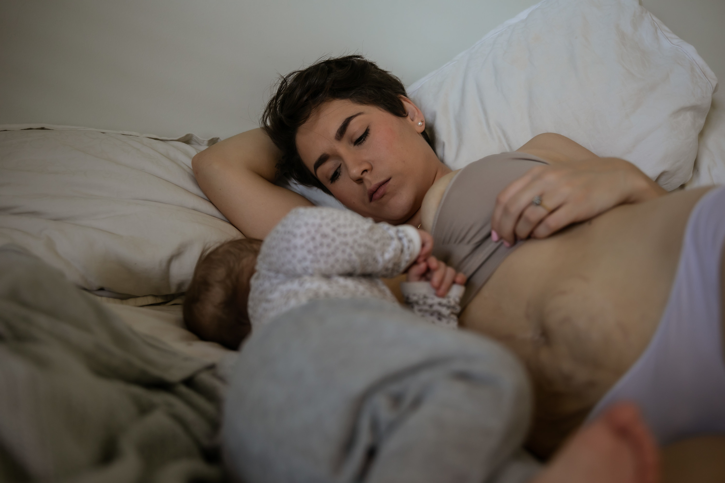 A moment in the postpartum life of a mother at home with her baby boy and toddler girl, she is tired and struggling to breastfeed. She is wearing postpartum briefs and you can clearly see the stretch marks on her belly from being pregnant