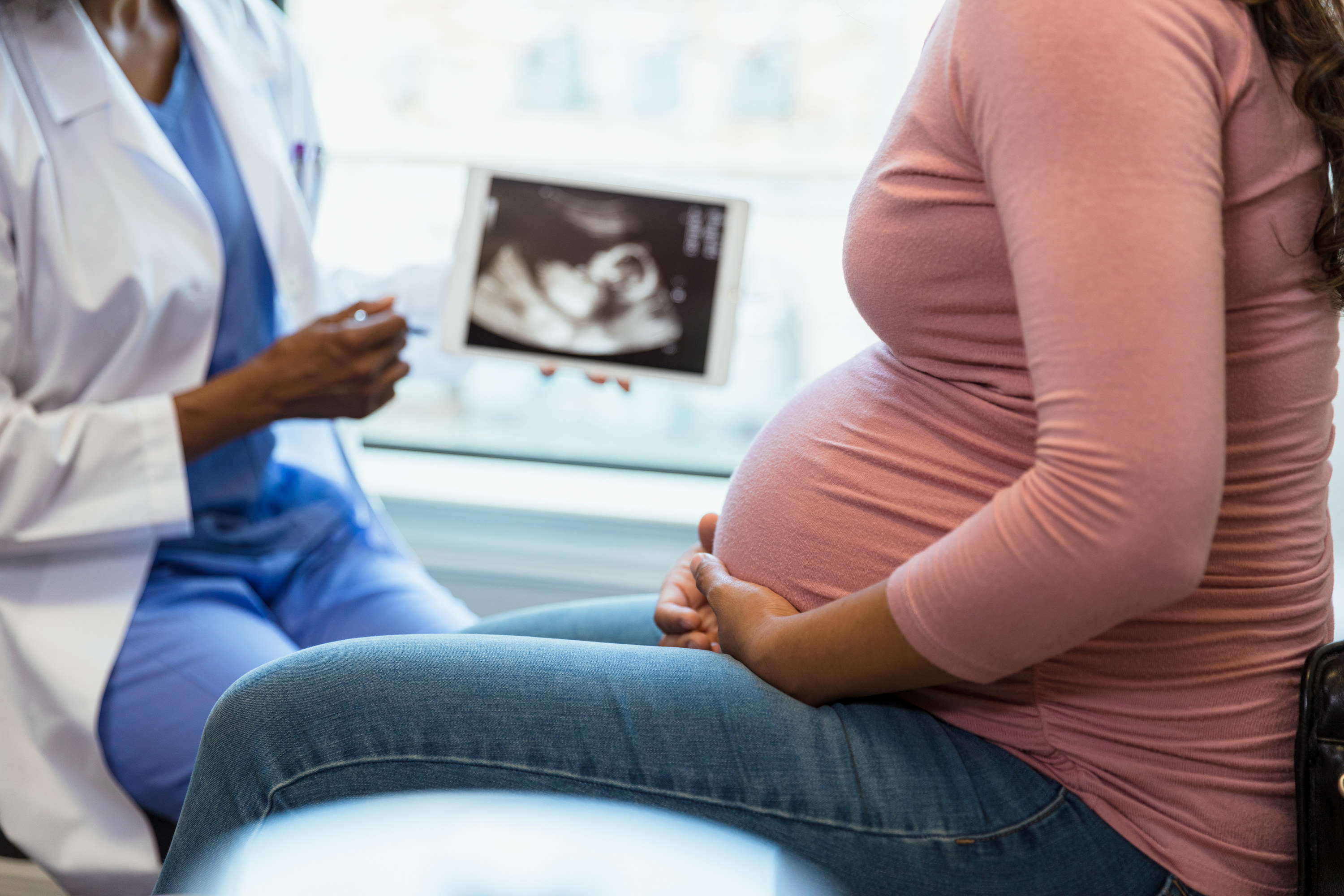 unrecognizable pregnant woman in the foreground as the unrecognizable doctor shows her an ultrasound on a digital tablet in the background