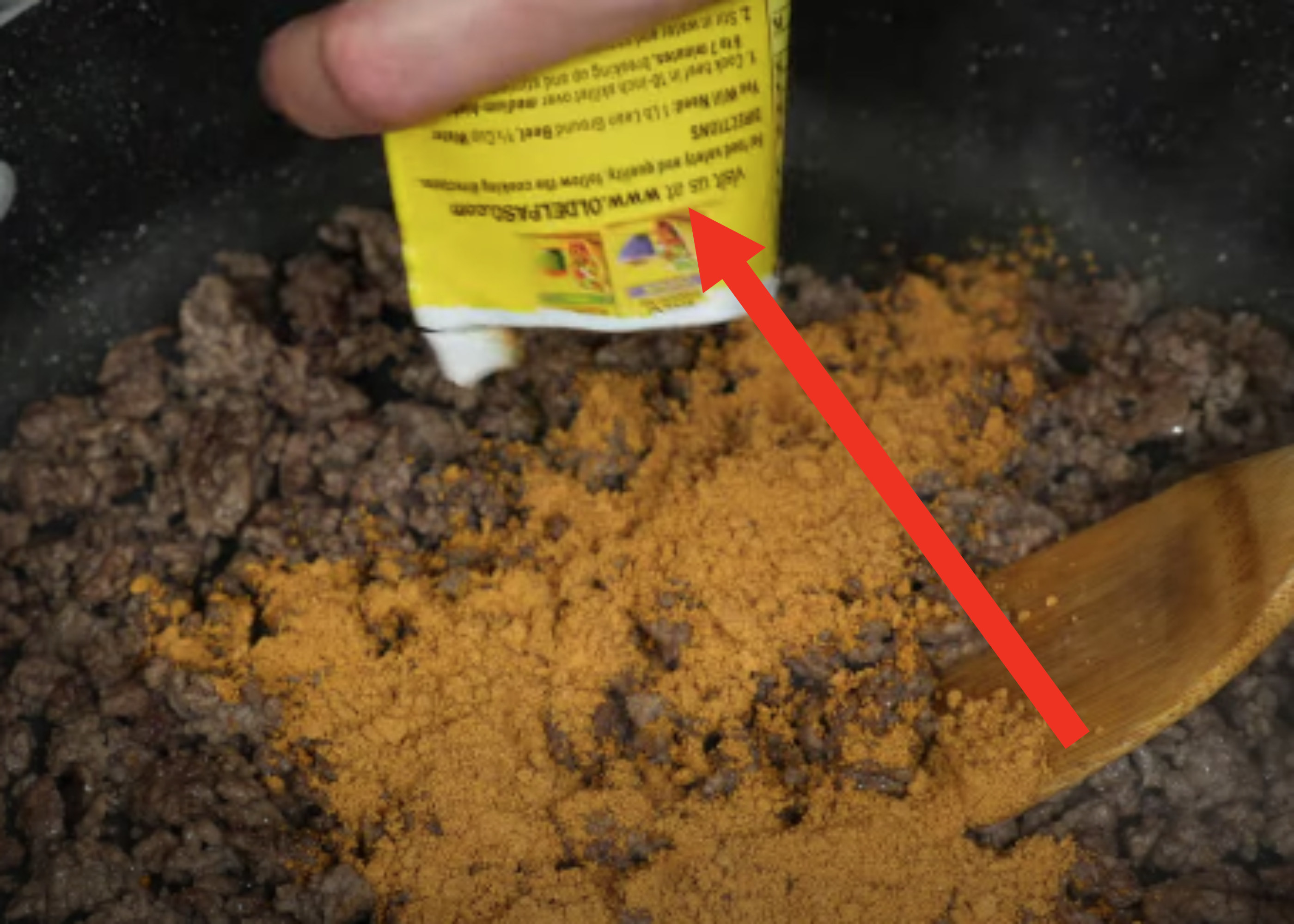 Emptying a packet of taco seasoning on a pan of beef