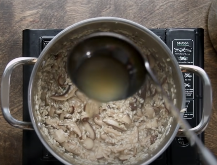 Adding a ladleful of stock to a pot of risotto