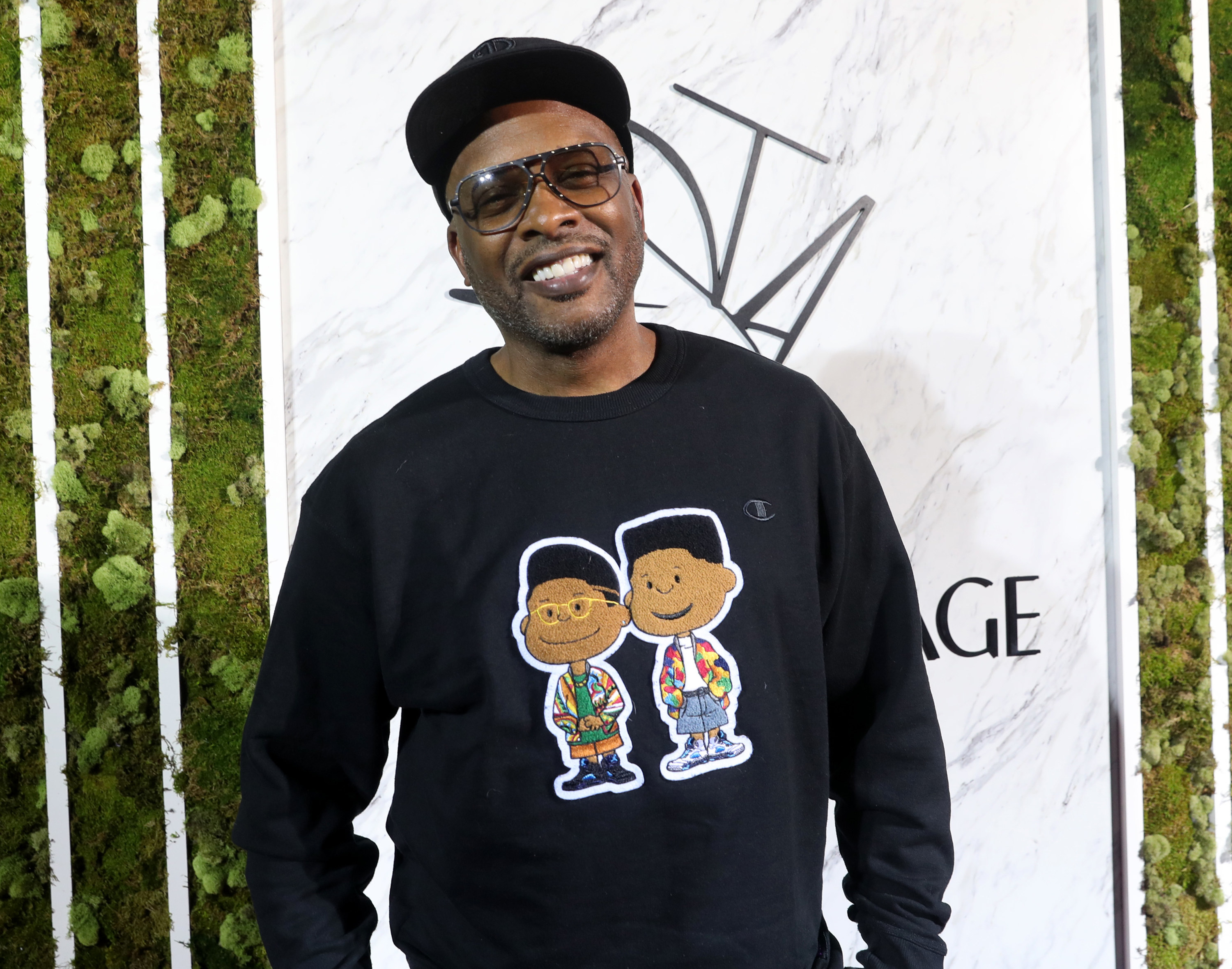 A smiling DJ Jazzy Jeff wearing a cap, glasses, and a sweatshirt