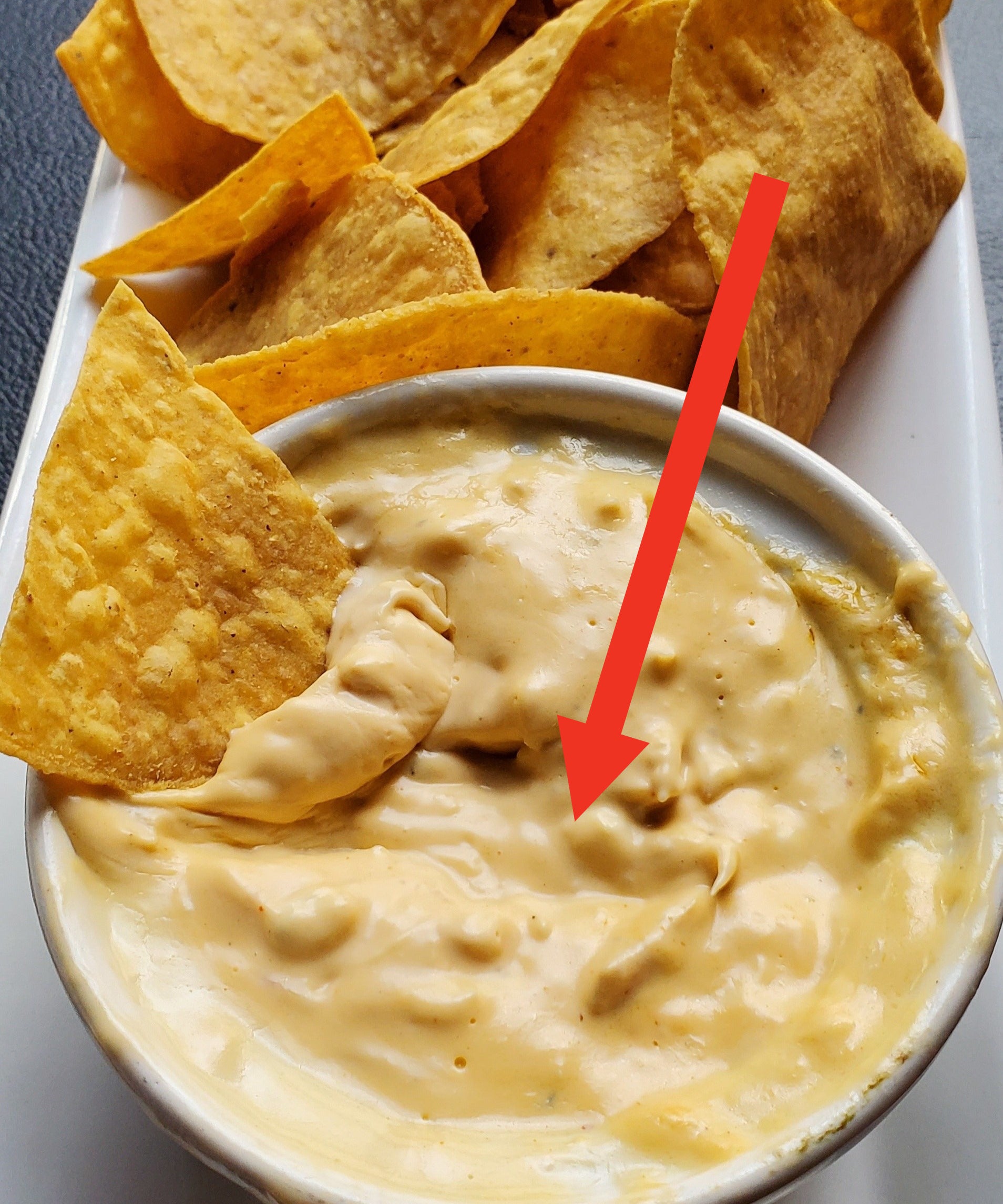 Arrow pointing to tortilla chip dipping into queso