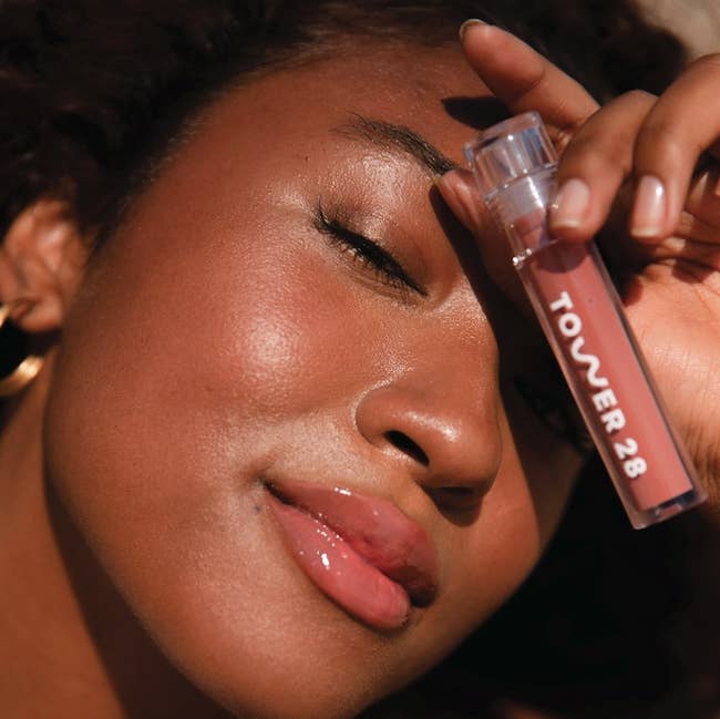 a model poses with this gloss tube while wearing the pink/brown-ish color 