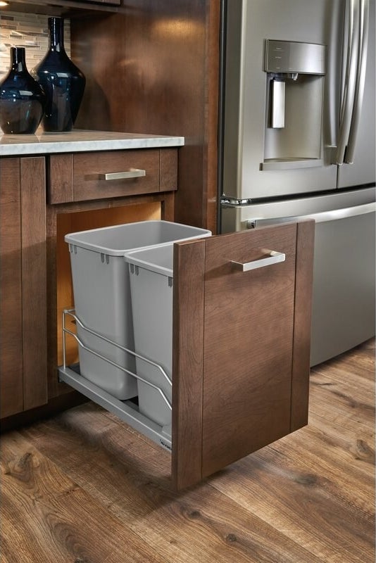 The pull out trash can in dark wooden cabinets