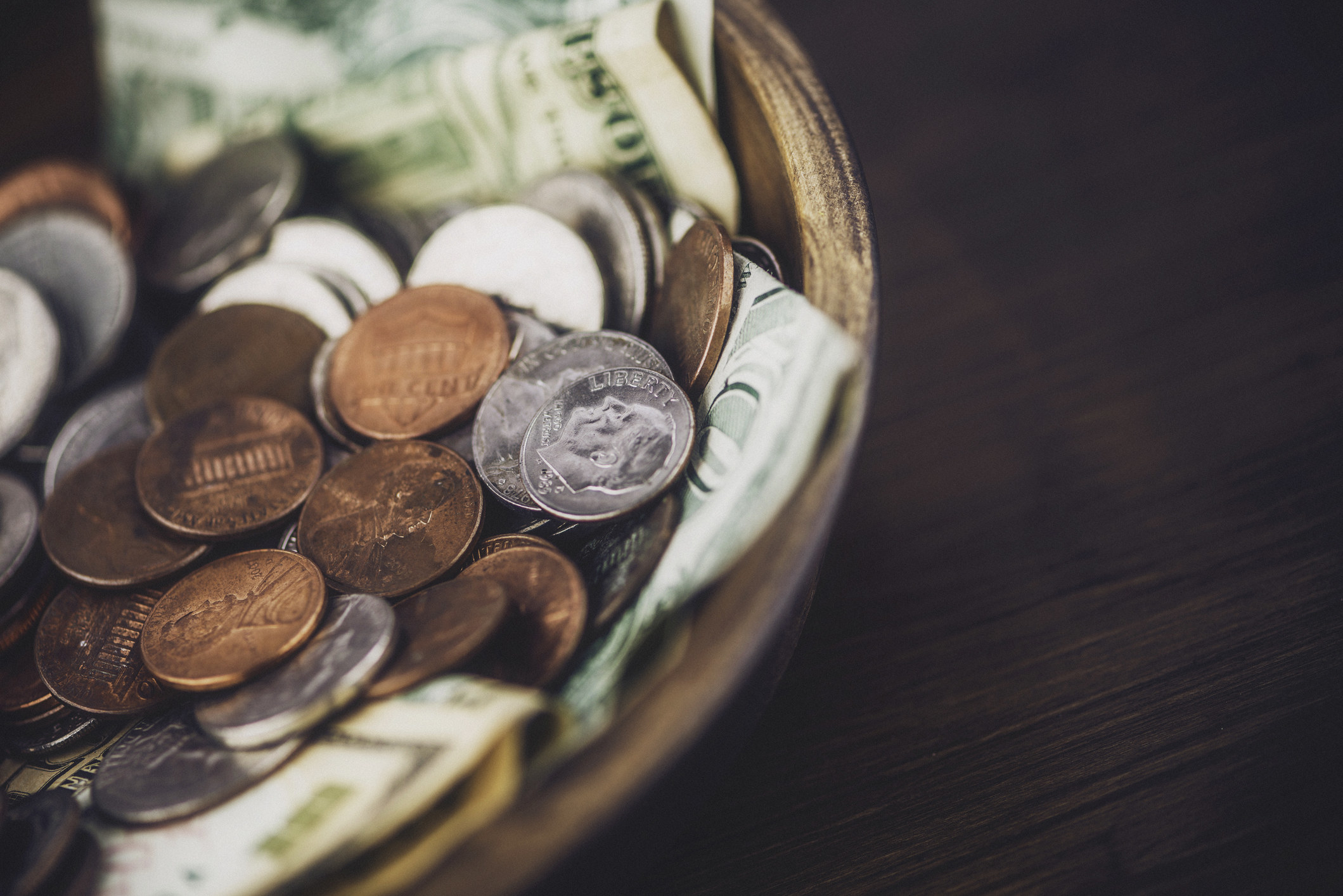 A wooden bowl filled with coins and bills