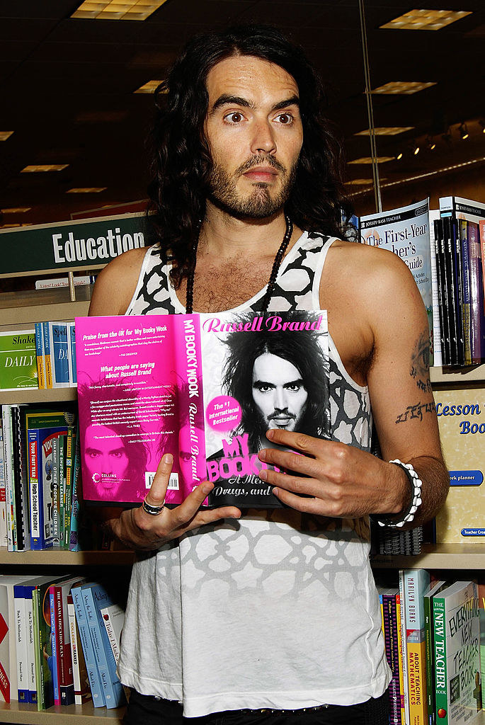 Russell Brand holding his book in a bookstore