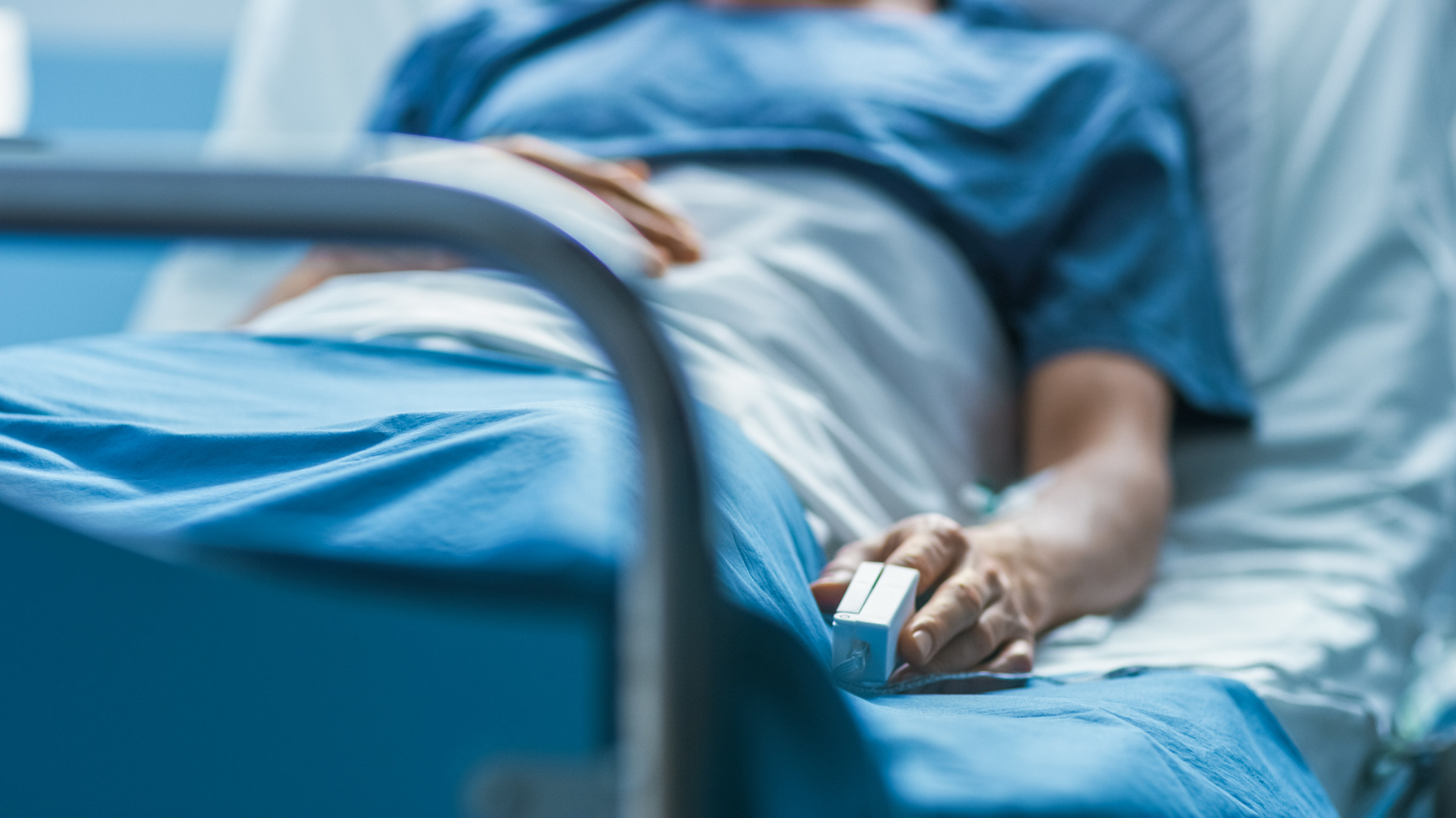 A patient lies in a hospital bed with a heart monitor on their finger