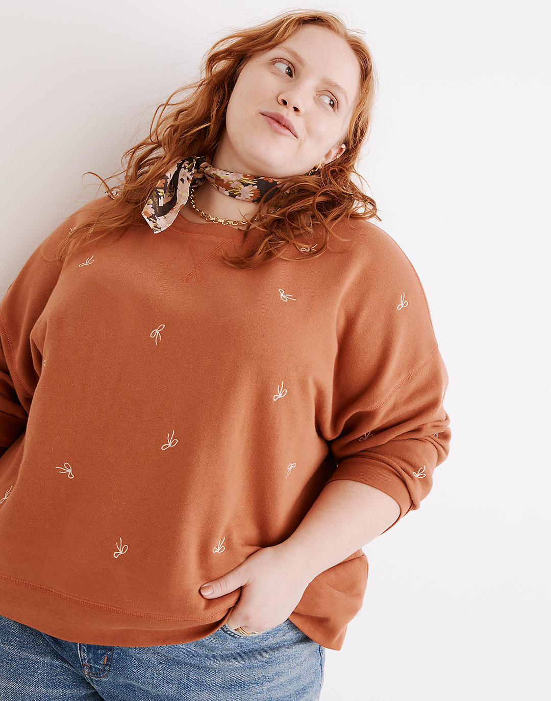 model in an orange sweatshirt with small lighter orange embroidered bows all over