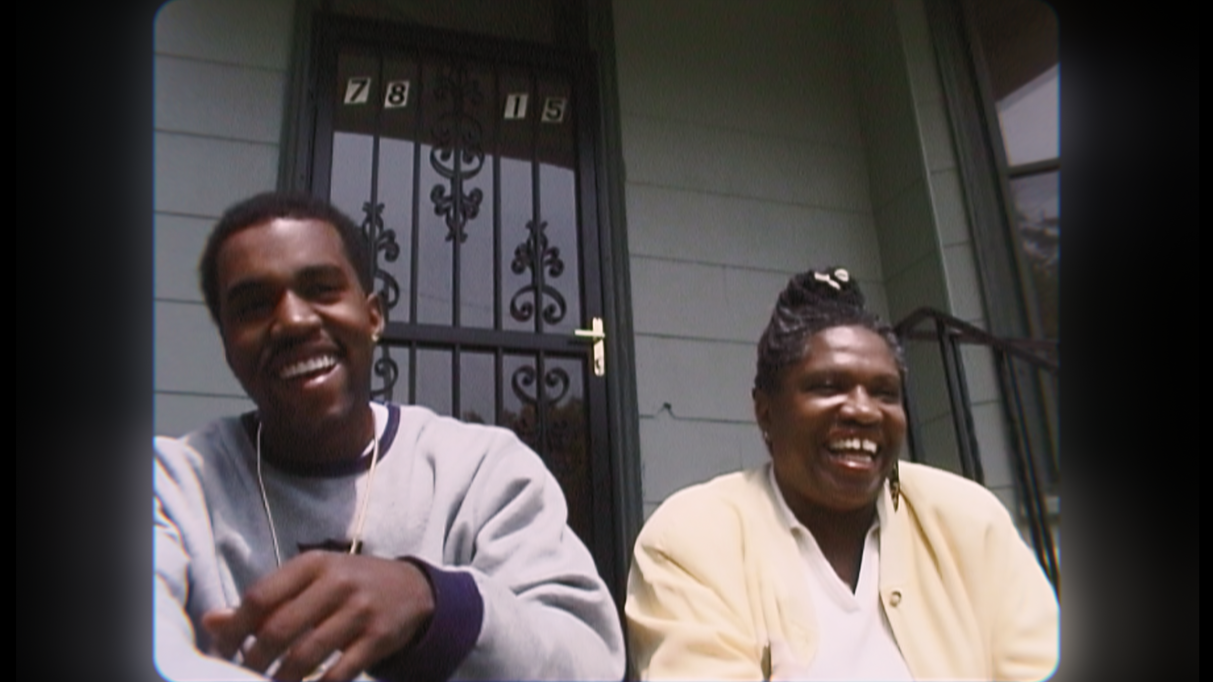 A younger Ye and his mother sit on a front porch laughing