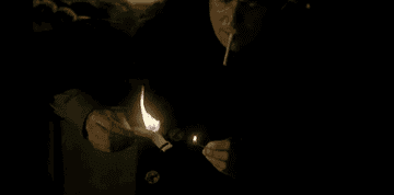 Gabriel Byrne as Keaton using a botch of matches to light a cigarette on a burning boat