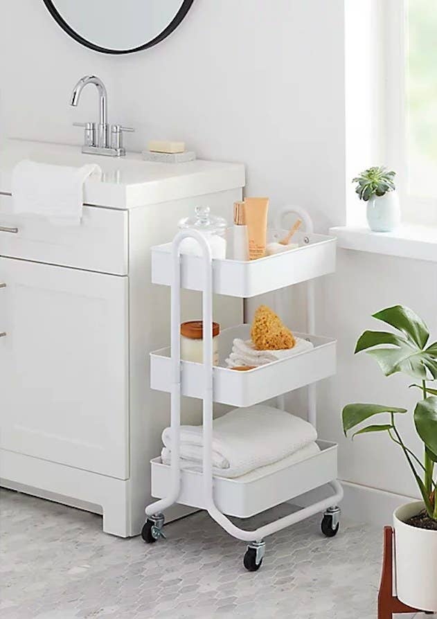 White cart filled with bathroom items next to a vanity