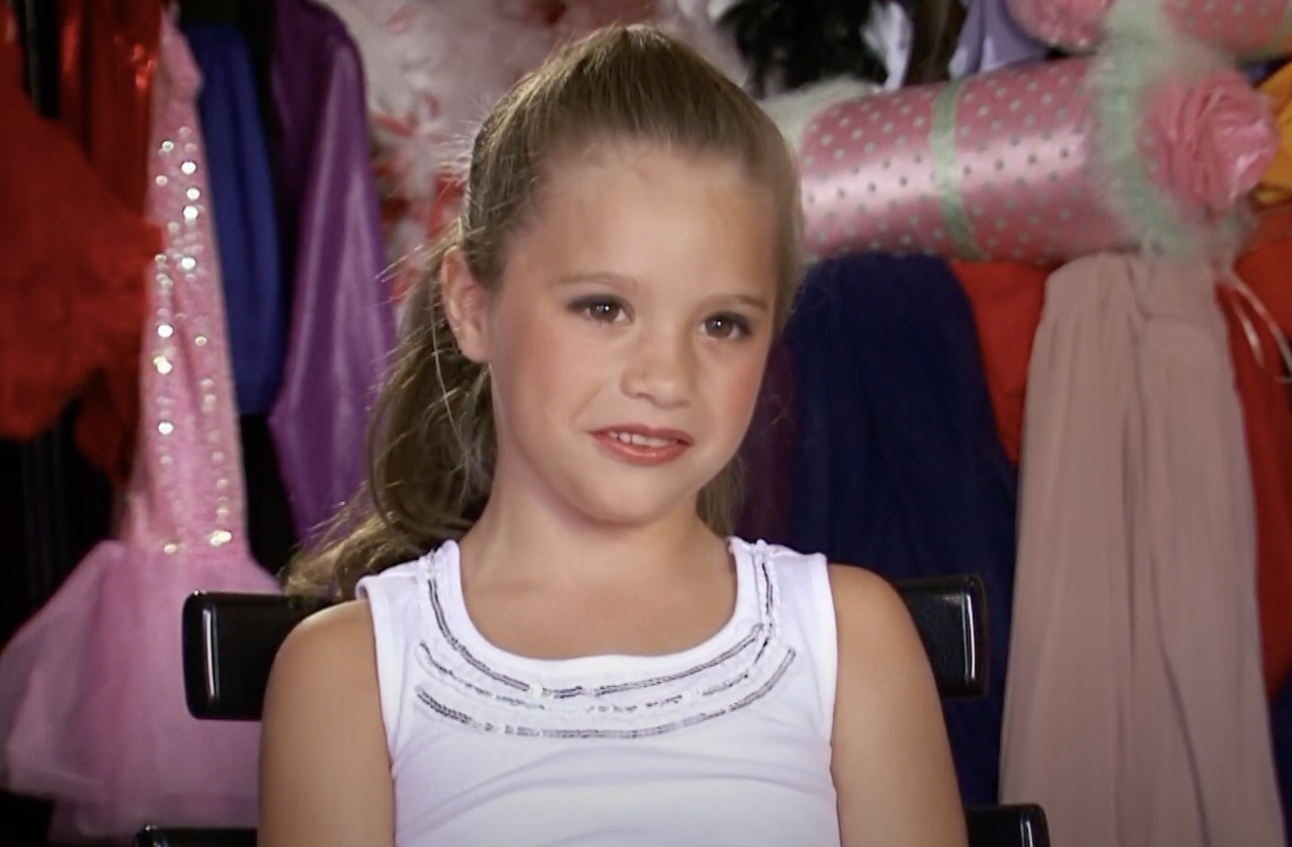 A young Mackenzie Ziegler in front of a rack of dresses