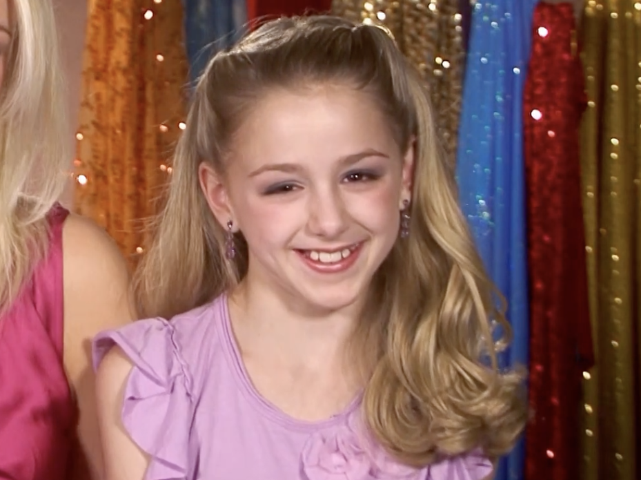 A young Chloe Lukasiak in front of a rack of dresses