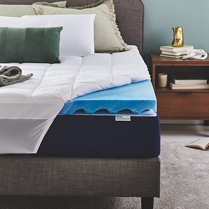 a fitted sheet being lifted to reveal a blue mattress topper on a bed