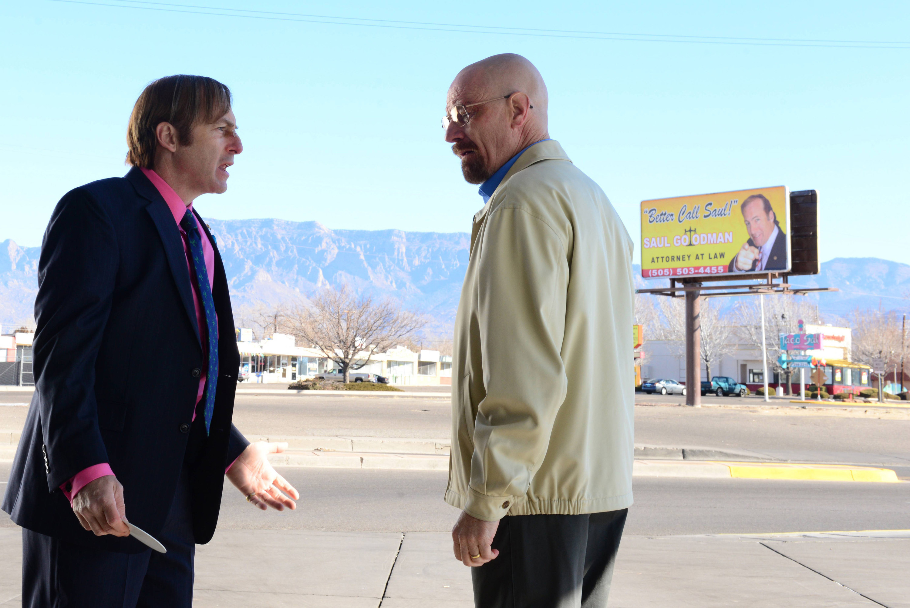 Saul and Walt argue in a parking lot underneath a better caul saul bulletin board