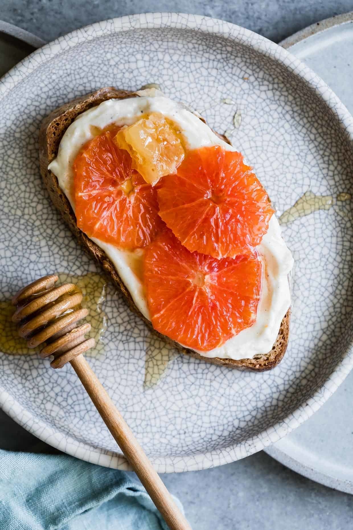 A slice of toast topped with ricotta, honey, and sliced orange.
