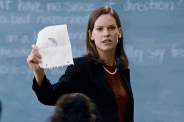 A close up of Hilary Swank as she holds up a piece of paper in front of a blackboard