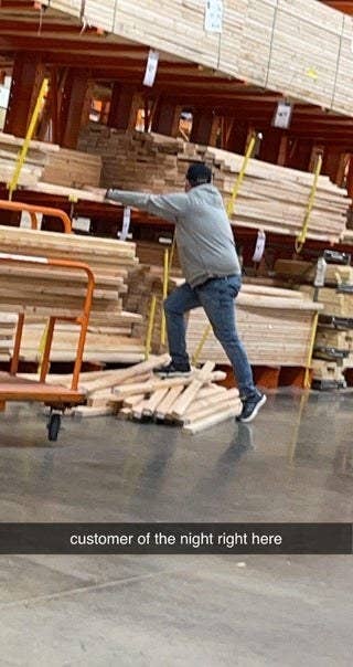 a man tries to use a pile of wood to reach other planks of wood on a shelf