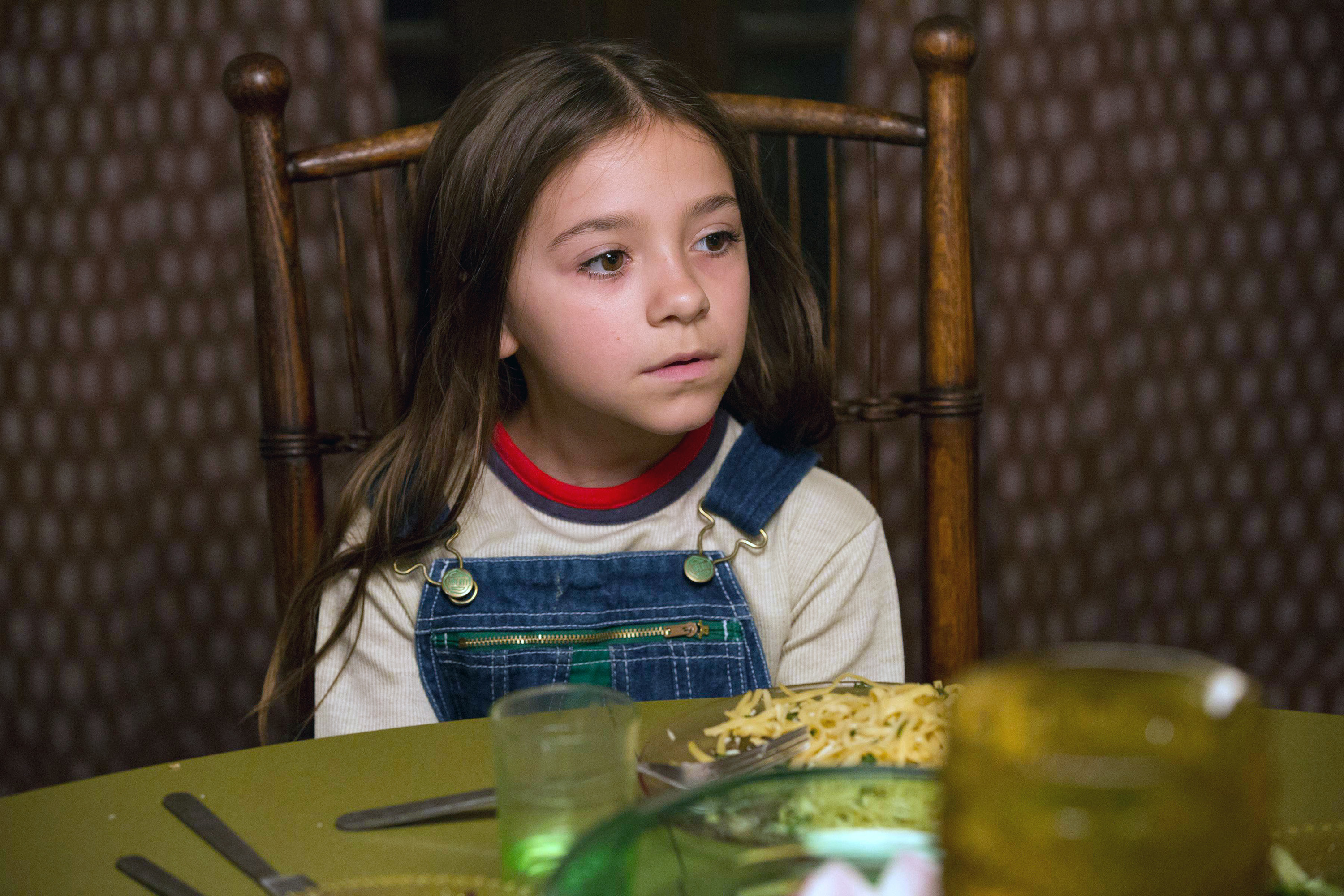 Young Olivia Edward as Duke in Better Things, wearing overalls at a table