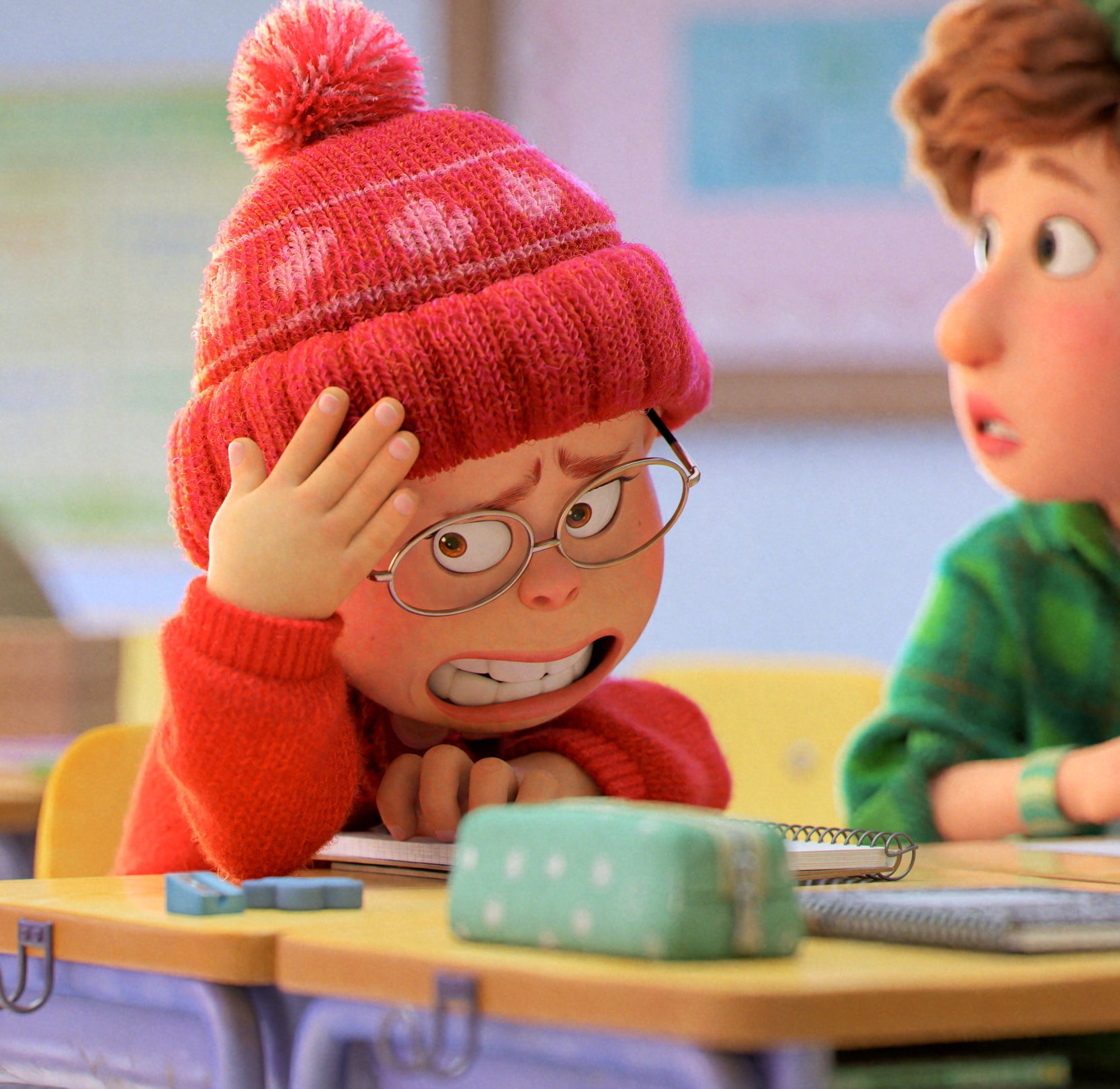The main character sitting at her desk in school wearing a Canadian toque and looking embarrassed