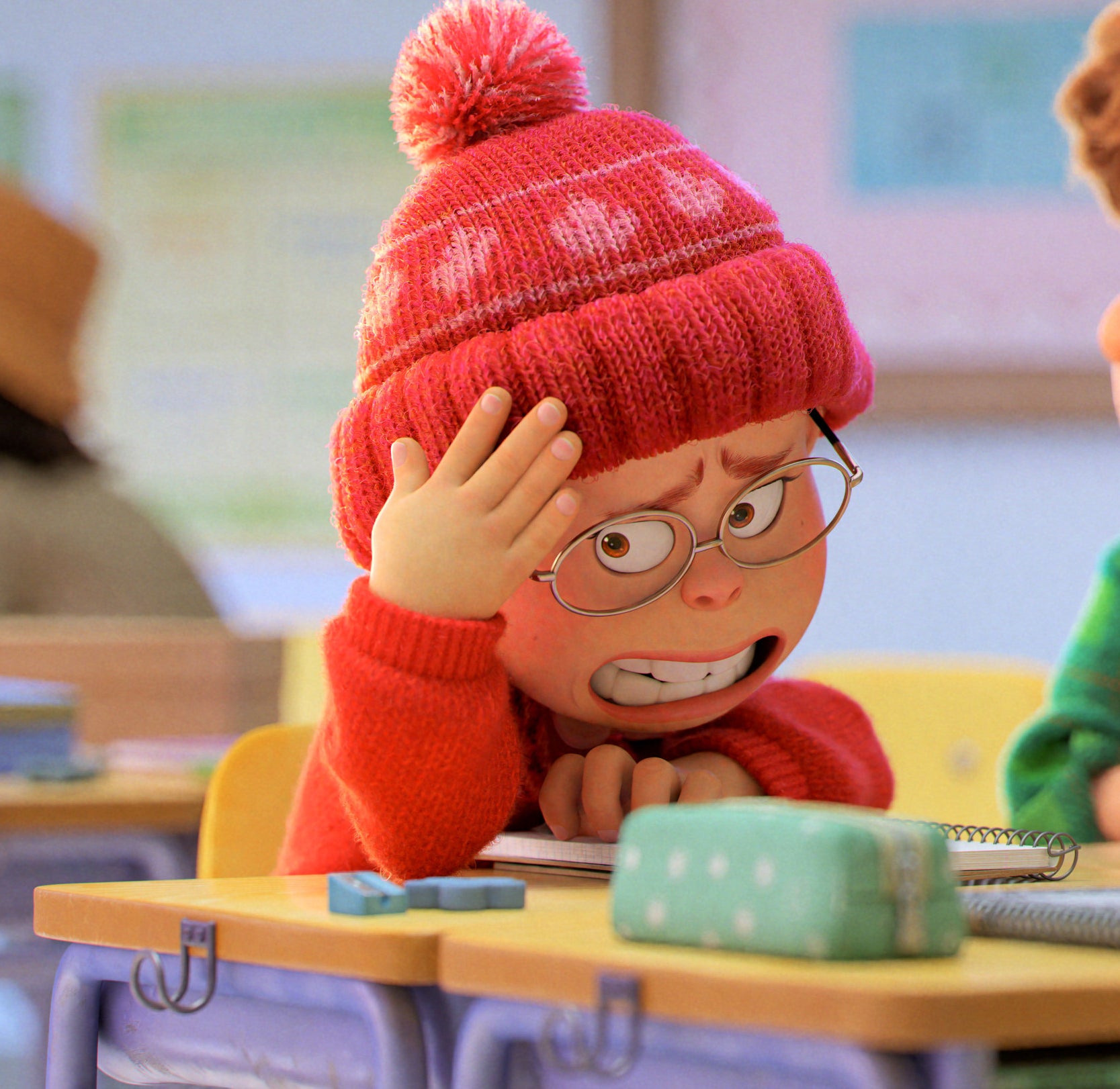 The main character sitting at her desk in school wearing a Canadian toque and looking embarrassed