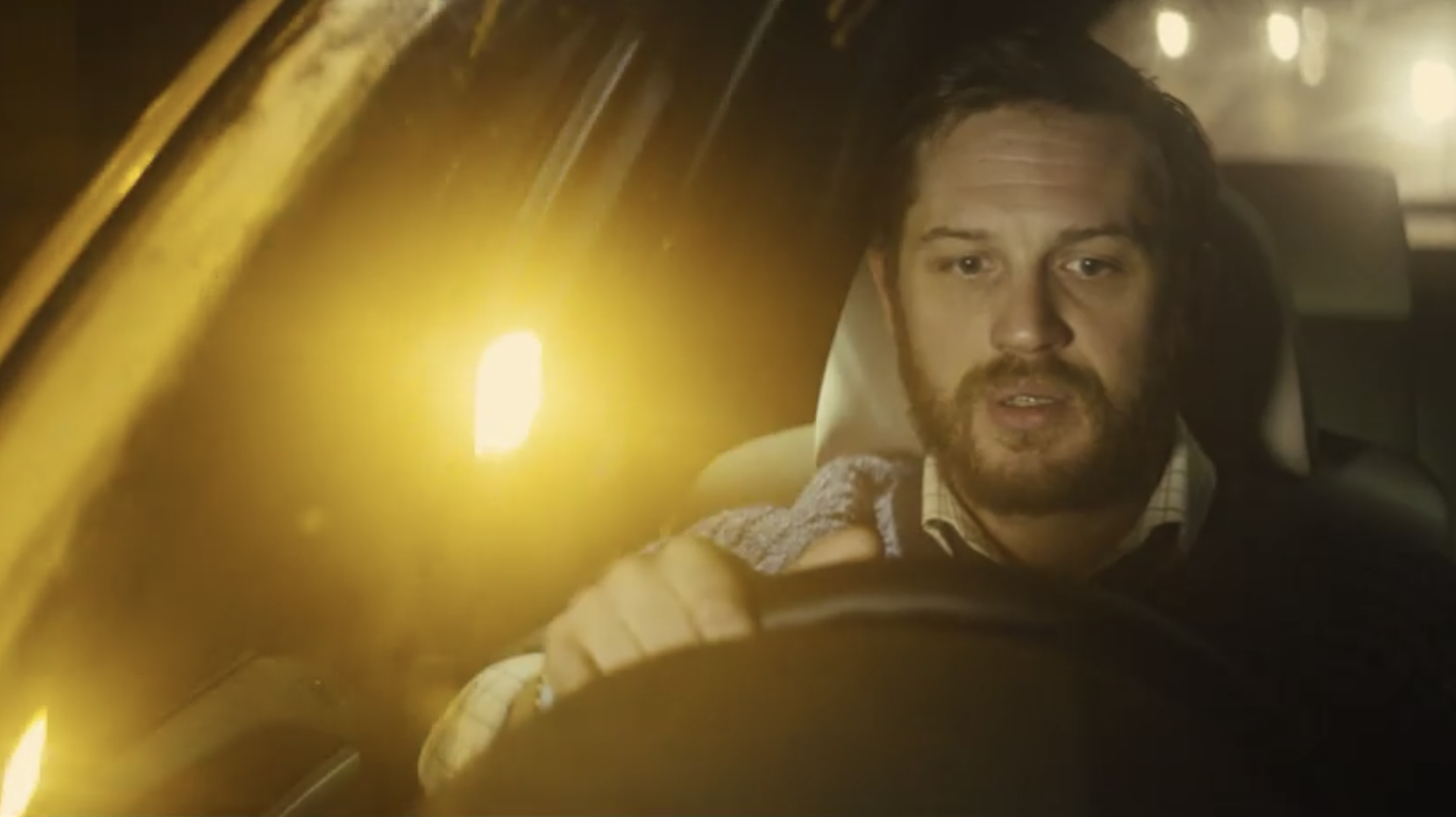 Tom Hardy driving at night with a bright headlight behind him