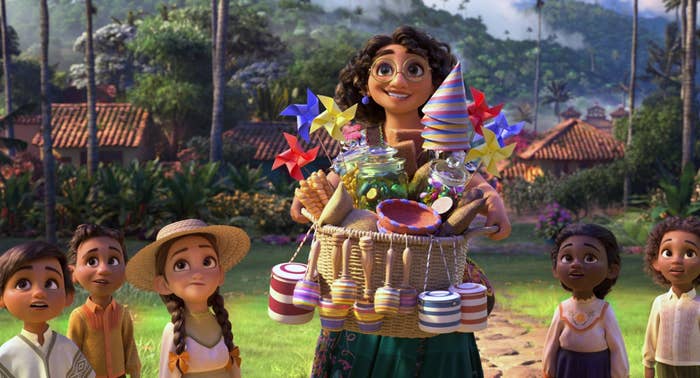 Mirabel smiling and holding a basket full of trinkets as she surrounded by children