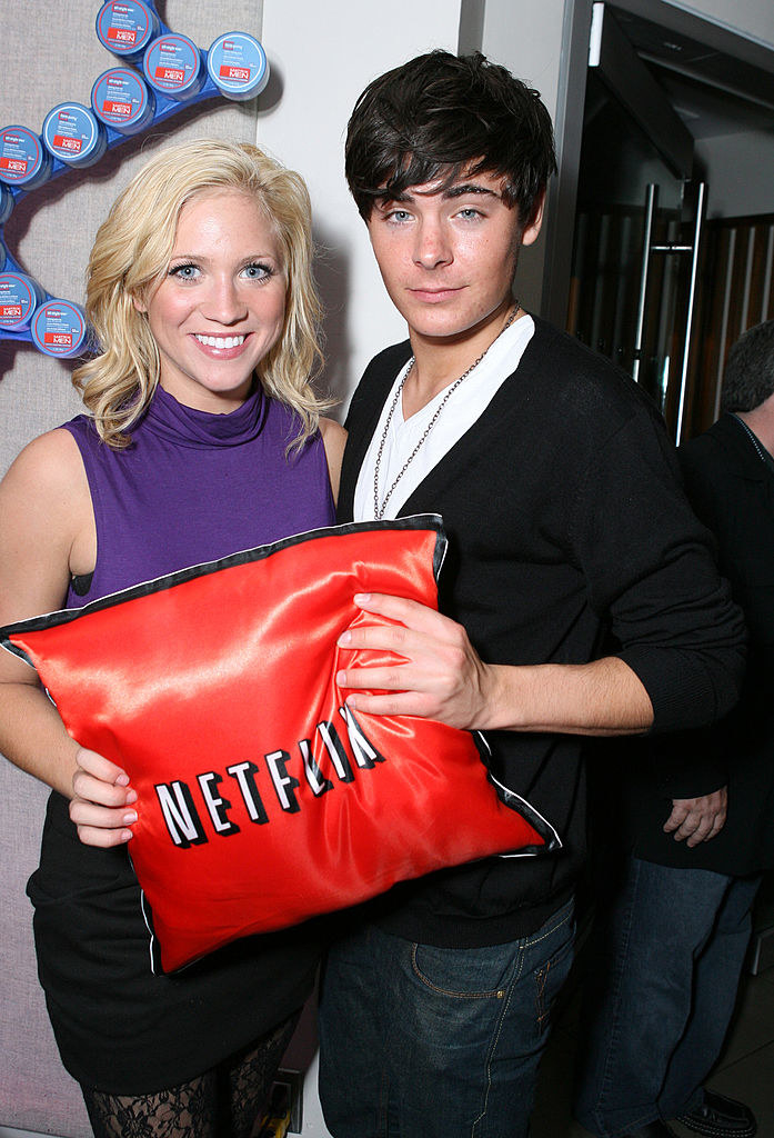 brittney and zac hold a red satin pillow with the netflix logo on it