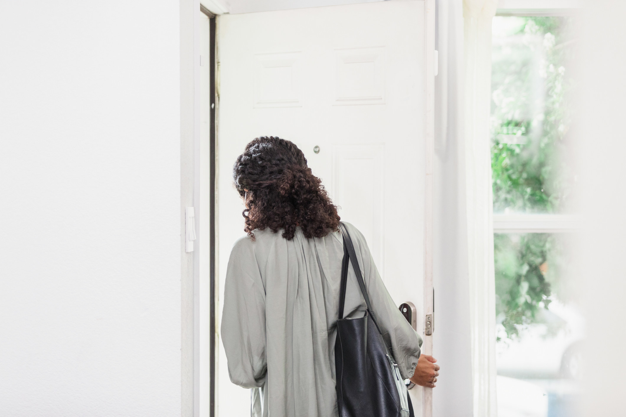 The unrecognizable young adult woman leaves her house carrying a purse. She is leaving through the front door.