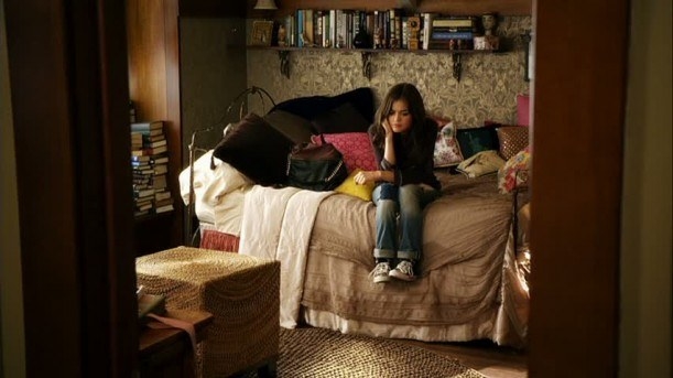 Aria sitting on her bed, surrounded by pillows, there are lots of books on the shelves