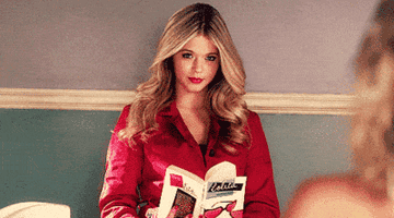 Alison wearing a red coat, reading the book Lolita, looking up and smiling