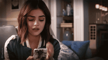 A GIF from the show, Aria looks at her phone and is visibly shocked, she puts her hand over her mouth