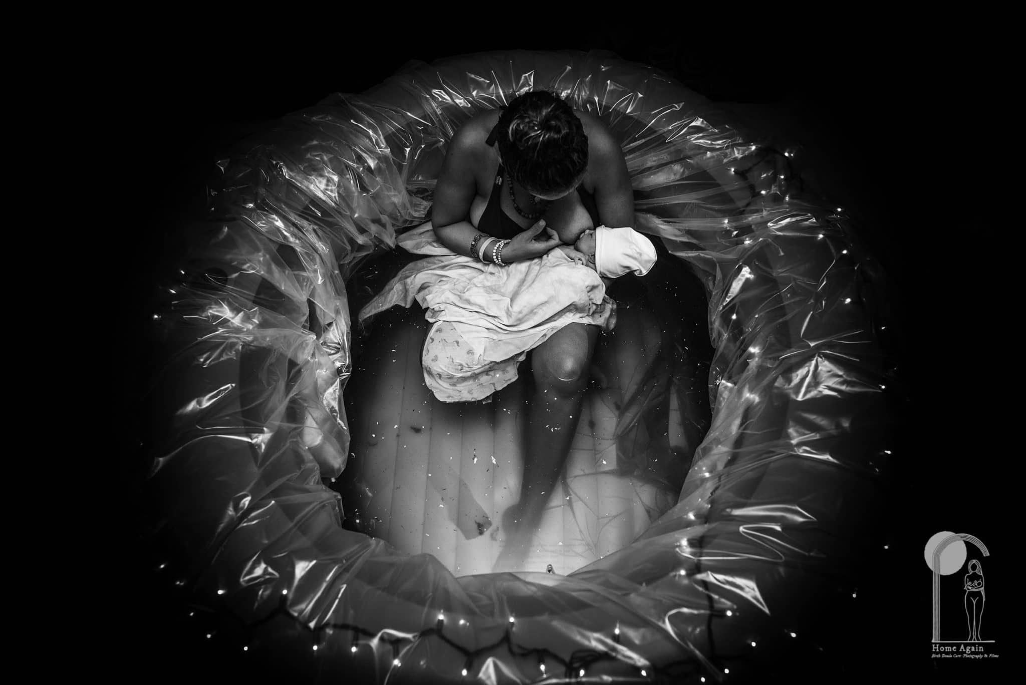 A woman holds her baby in a tub of water post birth