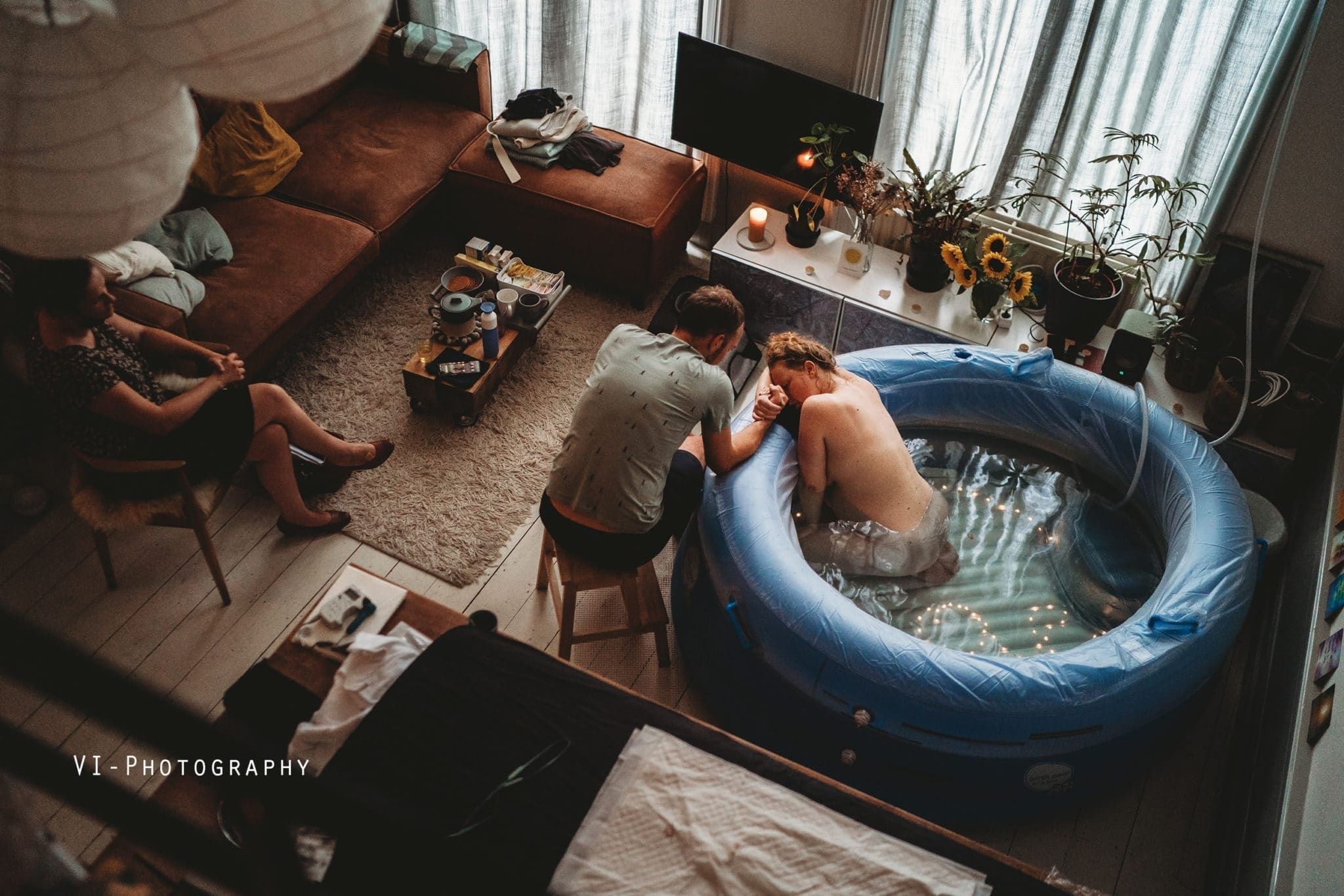 A woman sits in a tub of water setup in the living room as her husband holds her hand