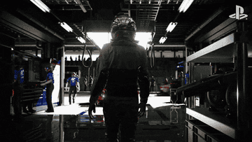 A race driver walking in a race garage with text appearing saying &quot;Gran Turismo is back&quot;