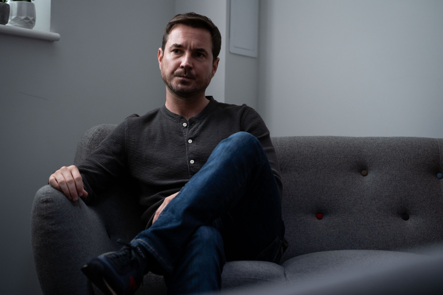 A worried looking Martin Compston as Bram Lawson sitting on a sofa
