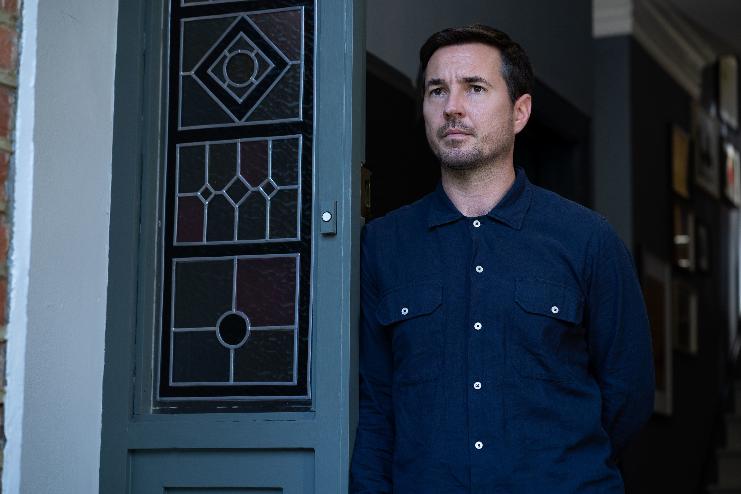 Martin Compston as Bram Lawson standing at the entrance of the house looking serious