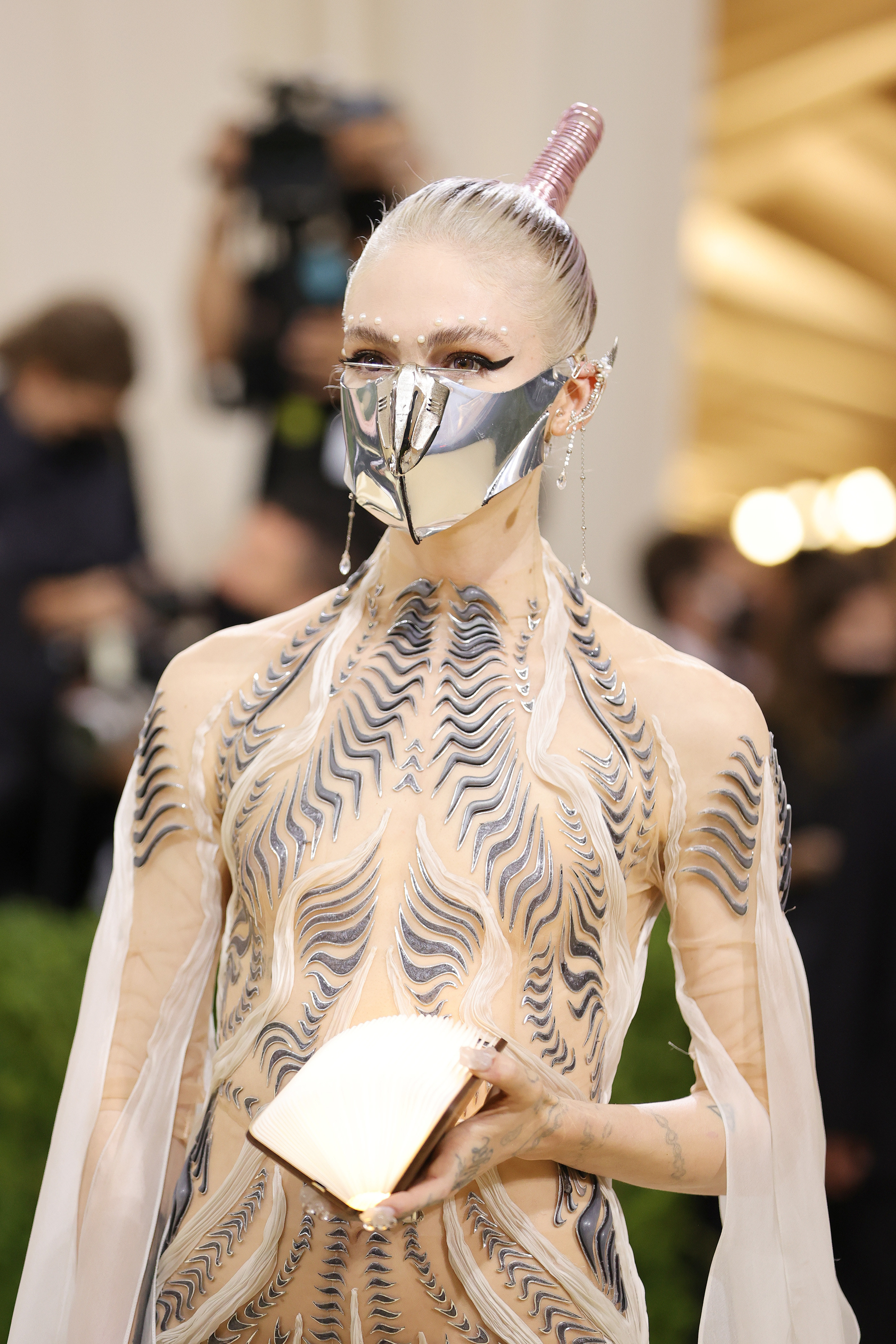 Grimes wear a metal face mask, and nude dress with lines detailing throughout