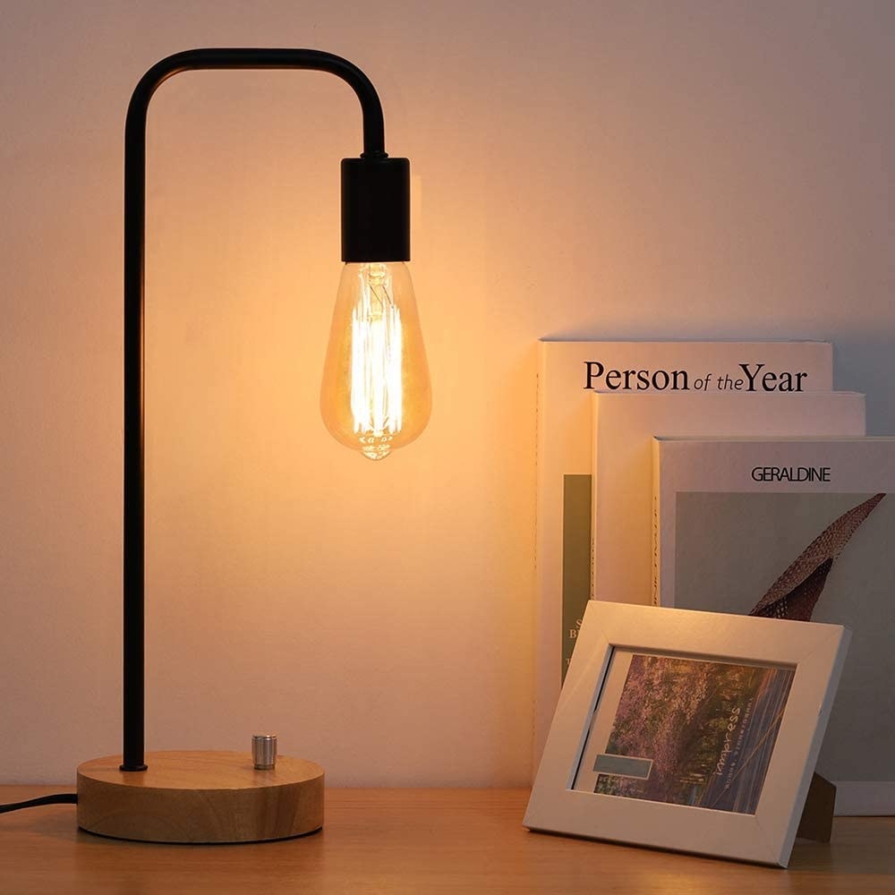The lamp on a table lit up next to a stack of books and a photo frame