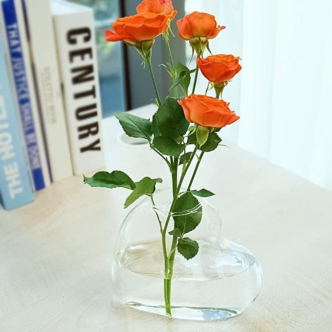 A heart-shaped vases on a table with a rose in it
