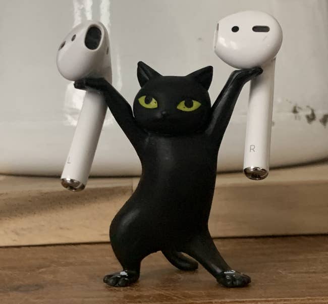 A reviewer's black cat figurine holding their Airpods