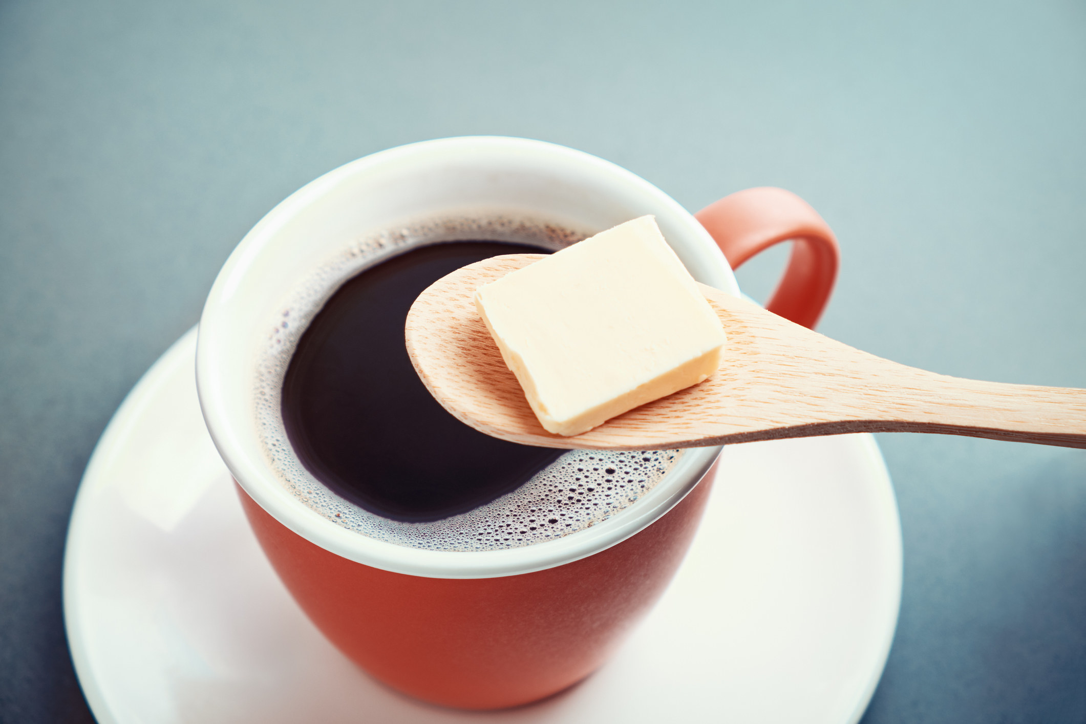 A pat of butter on top of a black cup of coffee