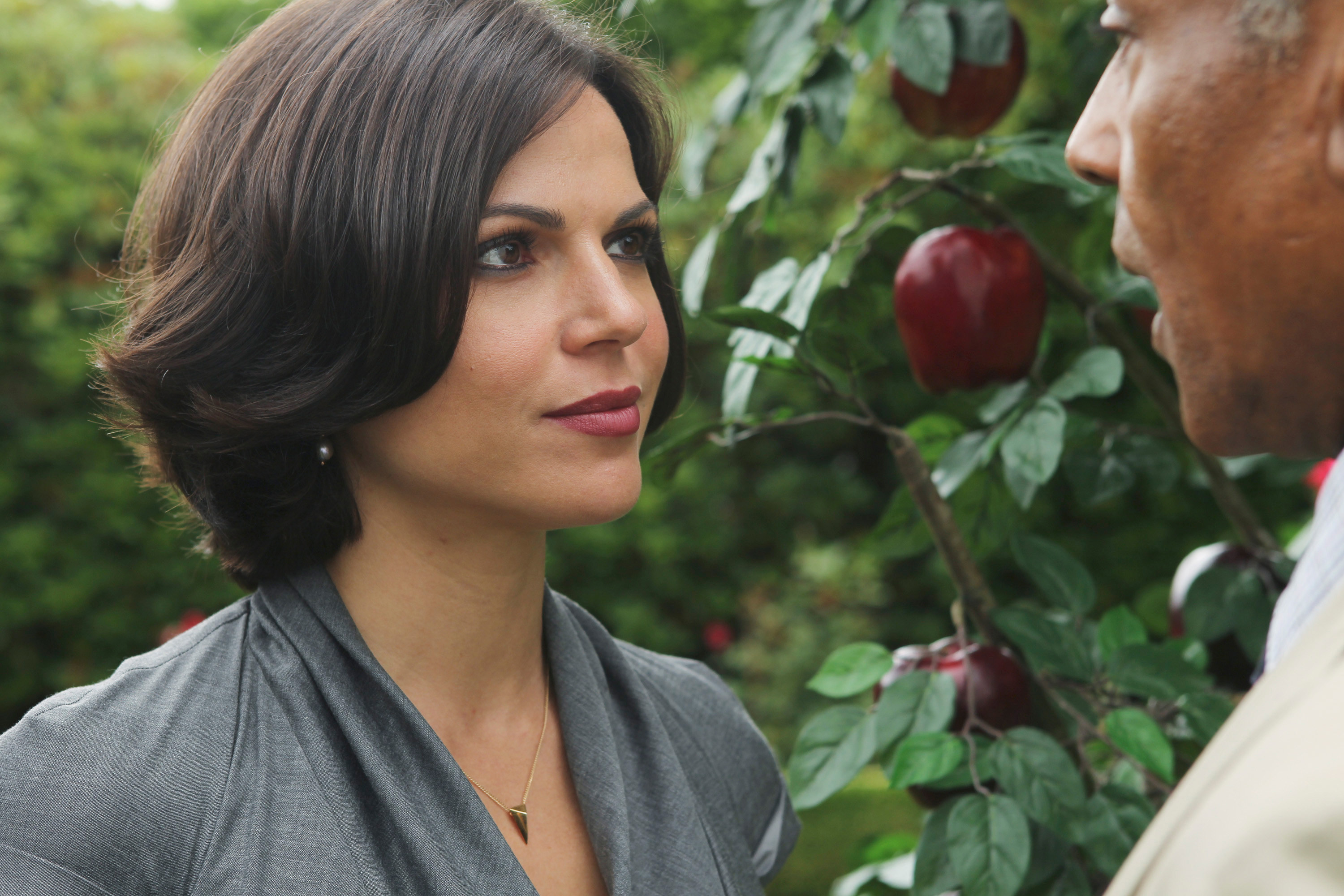 The Evil Queen grinning beside an apple tree