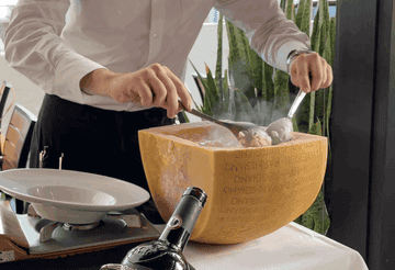 A member of the Arancino waitstaff mixing the risotto in a halved wheel of cheese