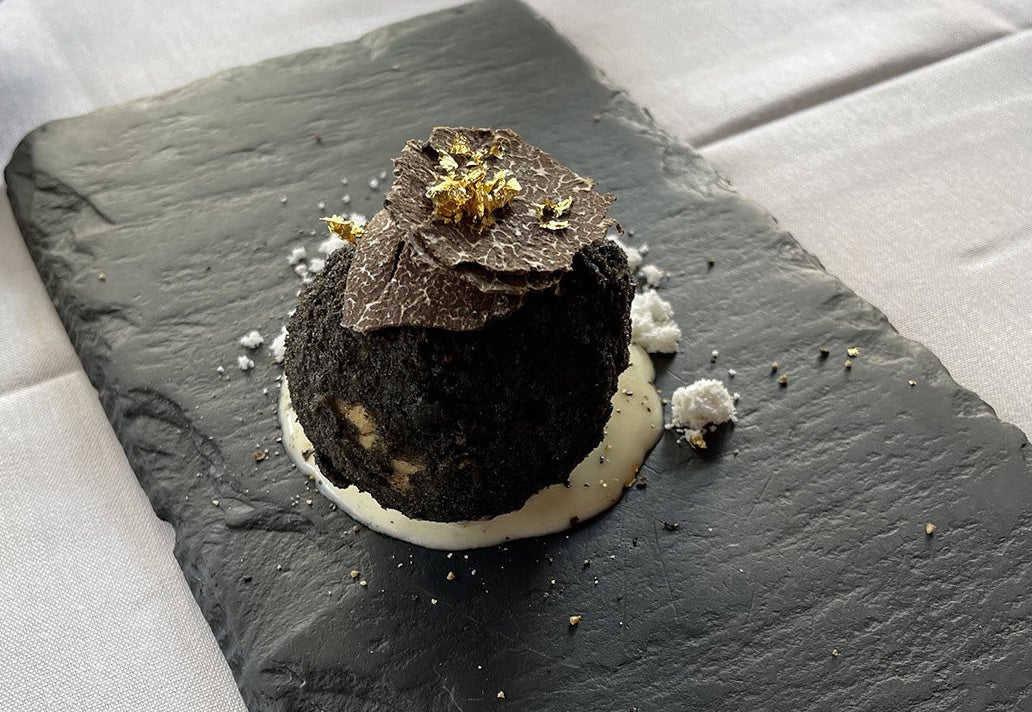 A fried risotto ball with black breading, shaved truffles, and gold foil on top