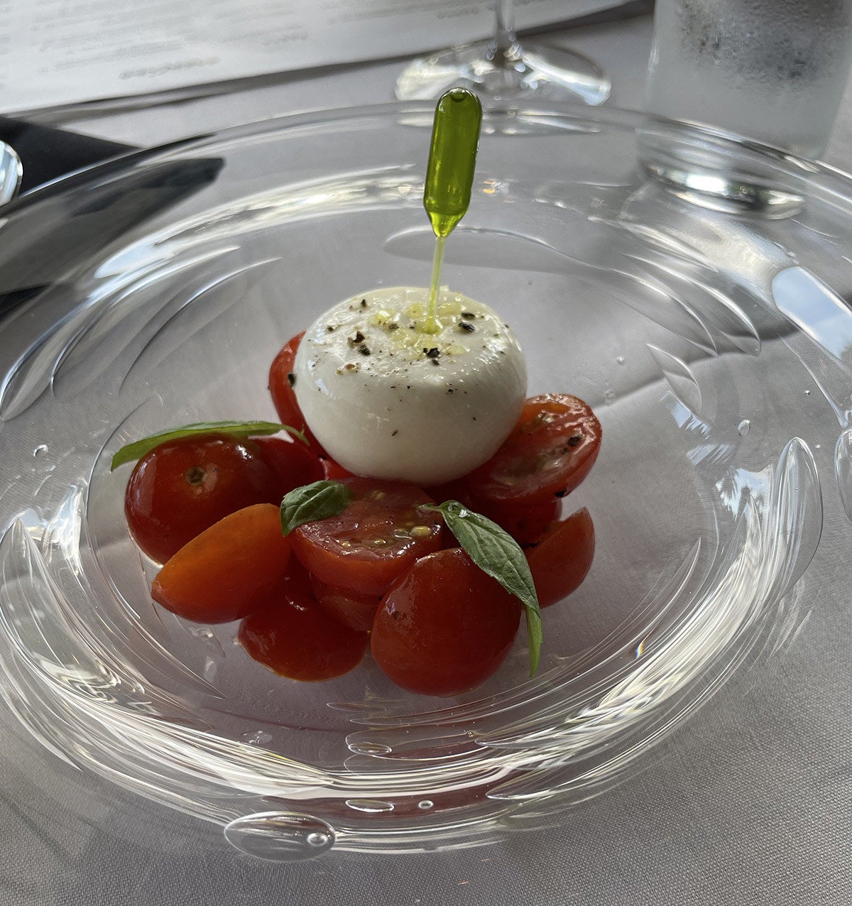 A glass plate with fresh tomatoes and burrata and a small dropper containing a greenish olive oil