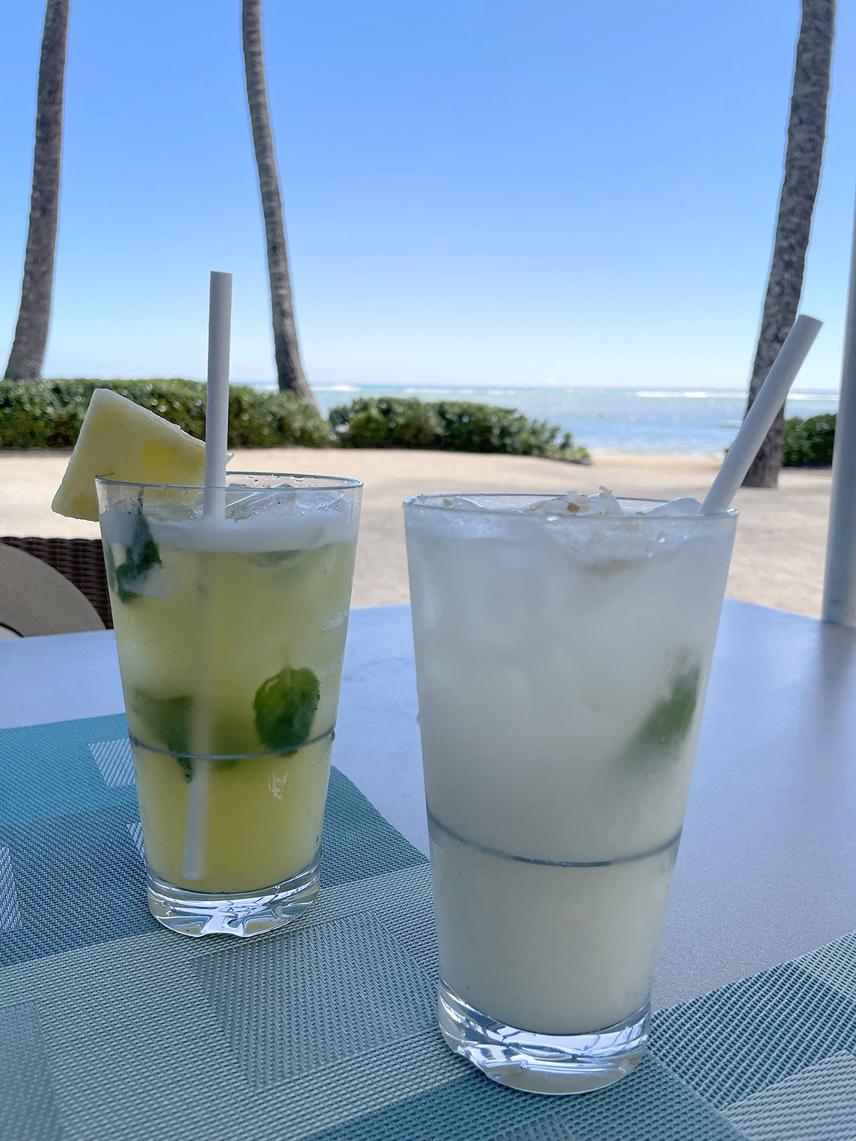 Two tropical-looking drinks on a table next to the beach